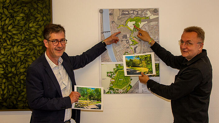 Zwei Männer zeigen auf einen Stadtplan und halten Visualisierungen eines Gartens hoch