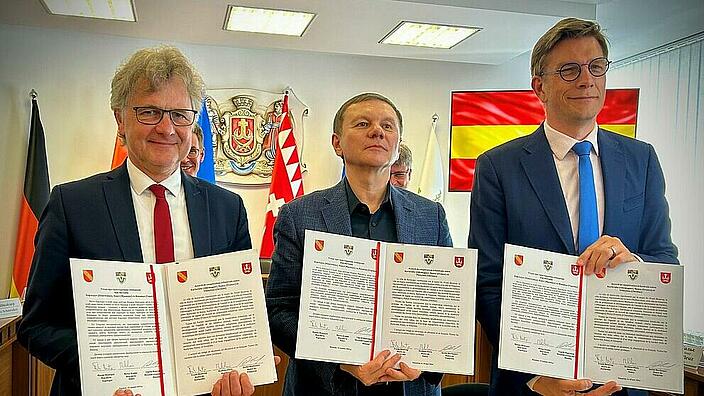 Drei Männer halten unterzeichnete Verträge hoch