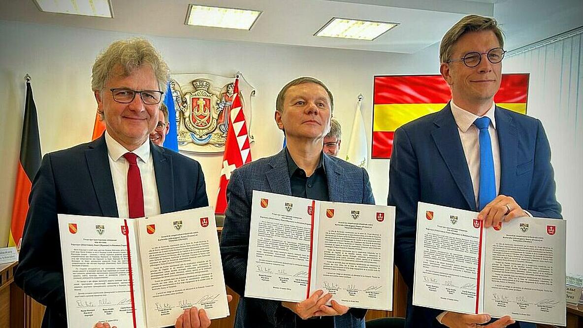 Drei Männer halten unterzeichnete Verträge hoch