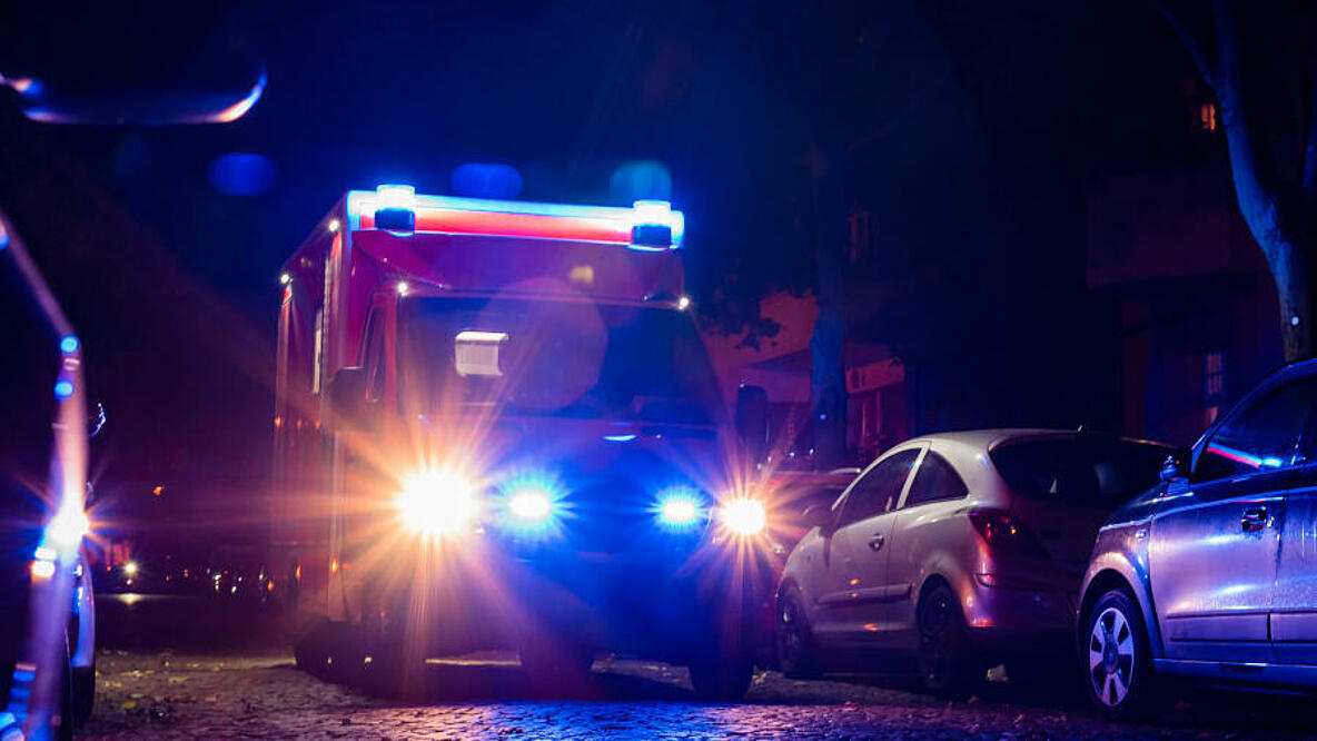 Rettungswagen mit Blaulicht fährt nachts an parkenden Autos vorbei